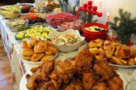 A festive holiday buffet table filled with fried chicken, salads, pastries, and colorful side dishes, all decorated with Christmas accents.