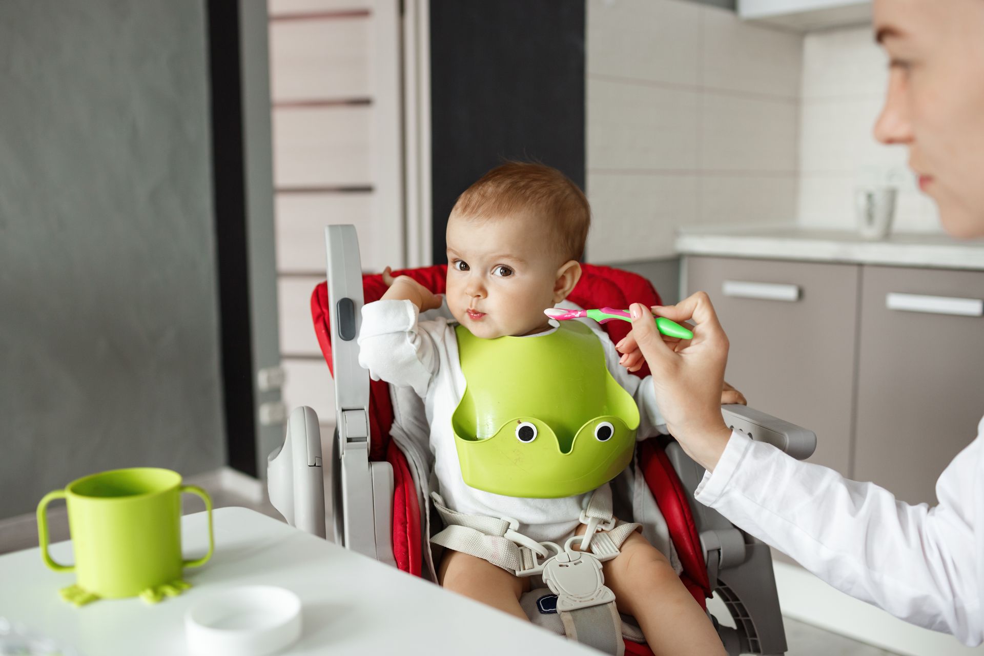 Maman qui donne à manger a son bébé qui refuse assis sur sa chaise haute et portant un bavoir imperméable en silicone. Maman qui donne à manger a son bébé qui refuse assis sur sa chaise haute et portant un bavoir imperméable en silicone.