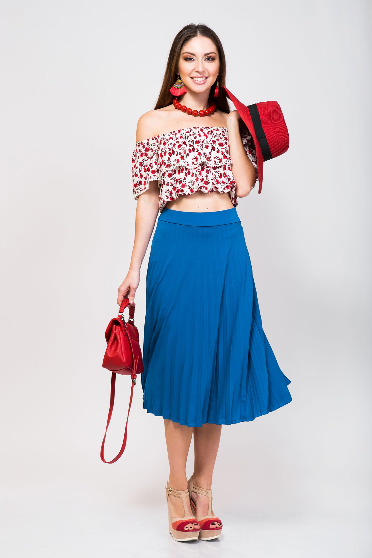 Une femme souriante, vêtue d'un haut court fleuri et d'une jupe plissée bleue et un sac rouge.. Une femme souriante, vêtue d'un haut court fleuri et d'une jupe plissée bleue et un sac rouge..