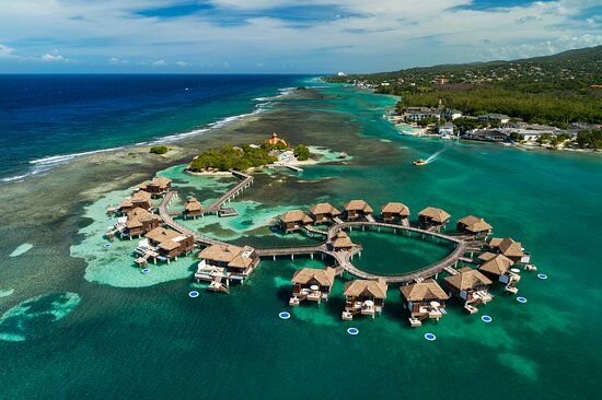 Aerial view of Sandals Royal Caribbean’s overwater bungalows connected by wooden walkways in clear turquoise waters in Montego Bay, Jamaica.