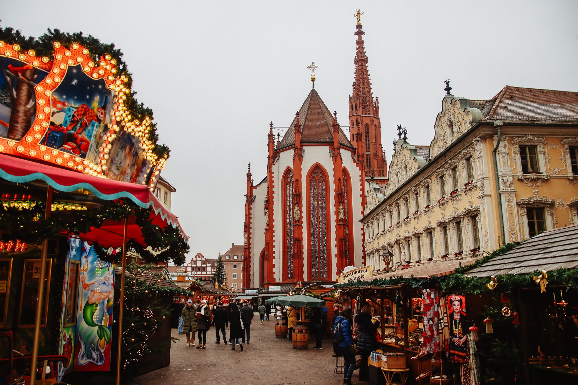 Festive stalls line the Würzburg Christmas Market in Germany, with glowing holiday decorations, shoppers strolling through the market, and historic church architecture rising in the background.