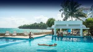 Guests relaxing in the oceanfront pool at Couples Tower Isle in Jamaica with palm trees and turquoise sea views.