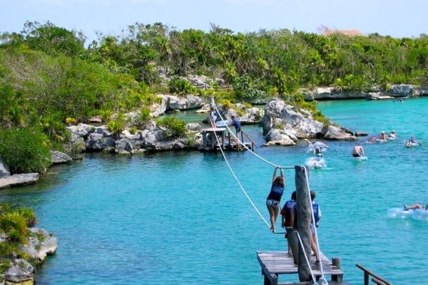 Travelers zipline and swim in the turquoise lagoon at Xel-Há Park, surrounded by lush tropical greenery and rocky shores in Mexico’s Riviera Maya. Travelers zipline and swim in the turquoise lagoon at Xel-Há Park, surrounded by lush tropical greenery and rocky shores in Mexico’s Riviera Maya.