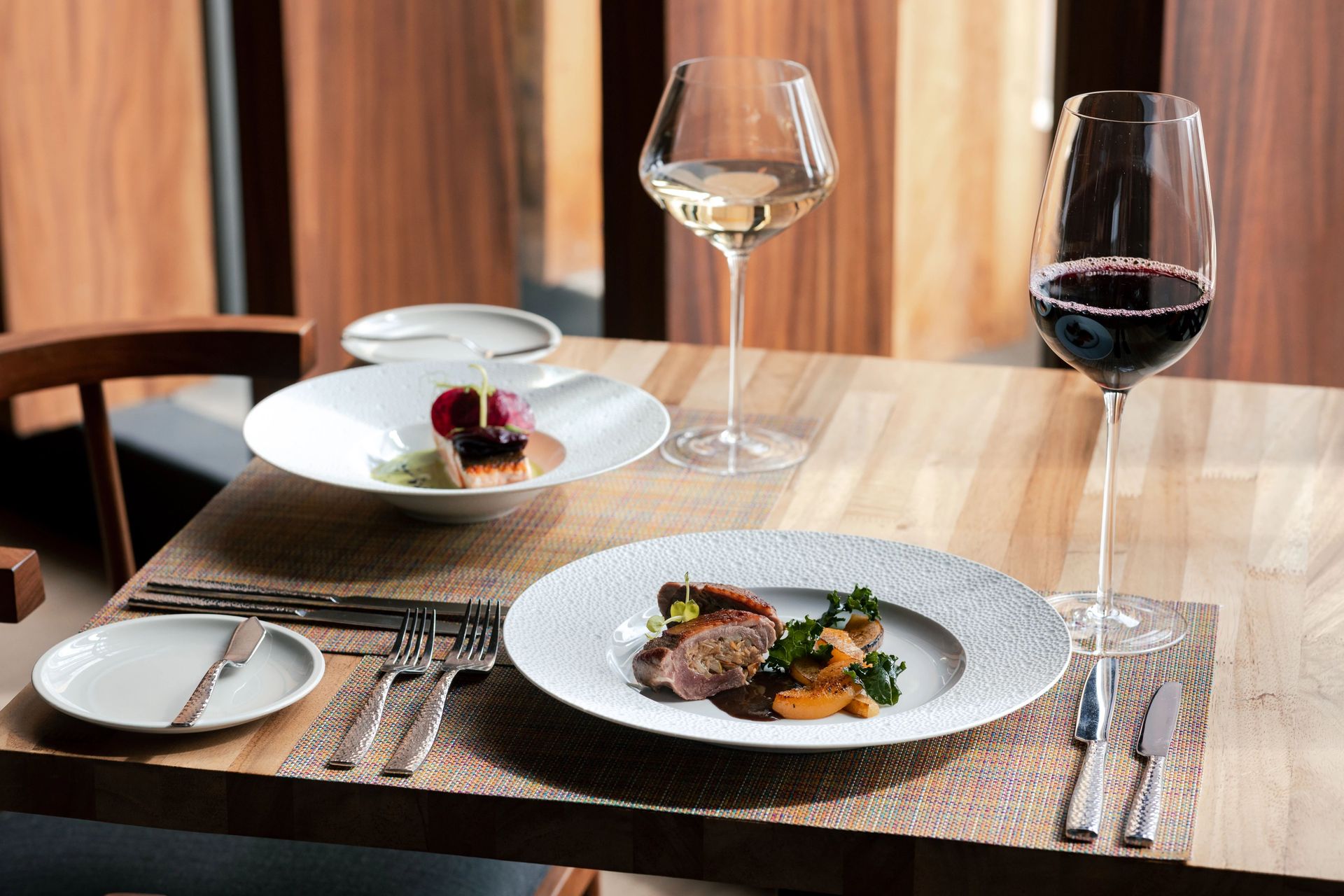 Elegant table setting with gourmet dishes and glasses of red and white wine.