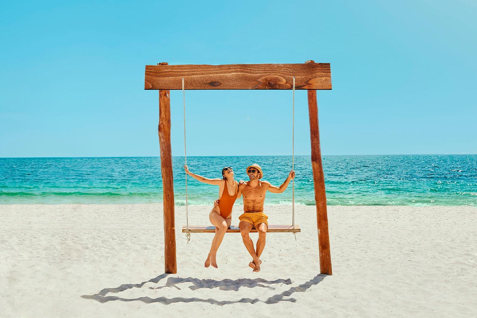 Couple relaxing on a wooden beach swing overlooking turquoise ocean