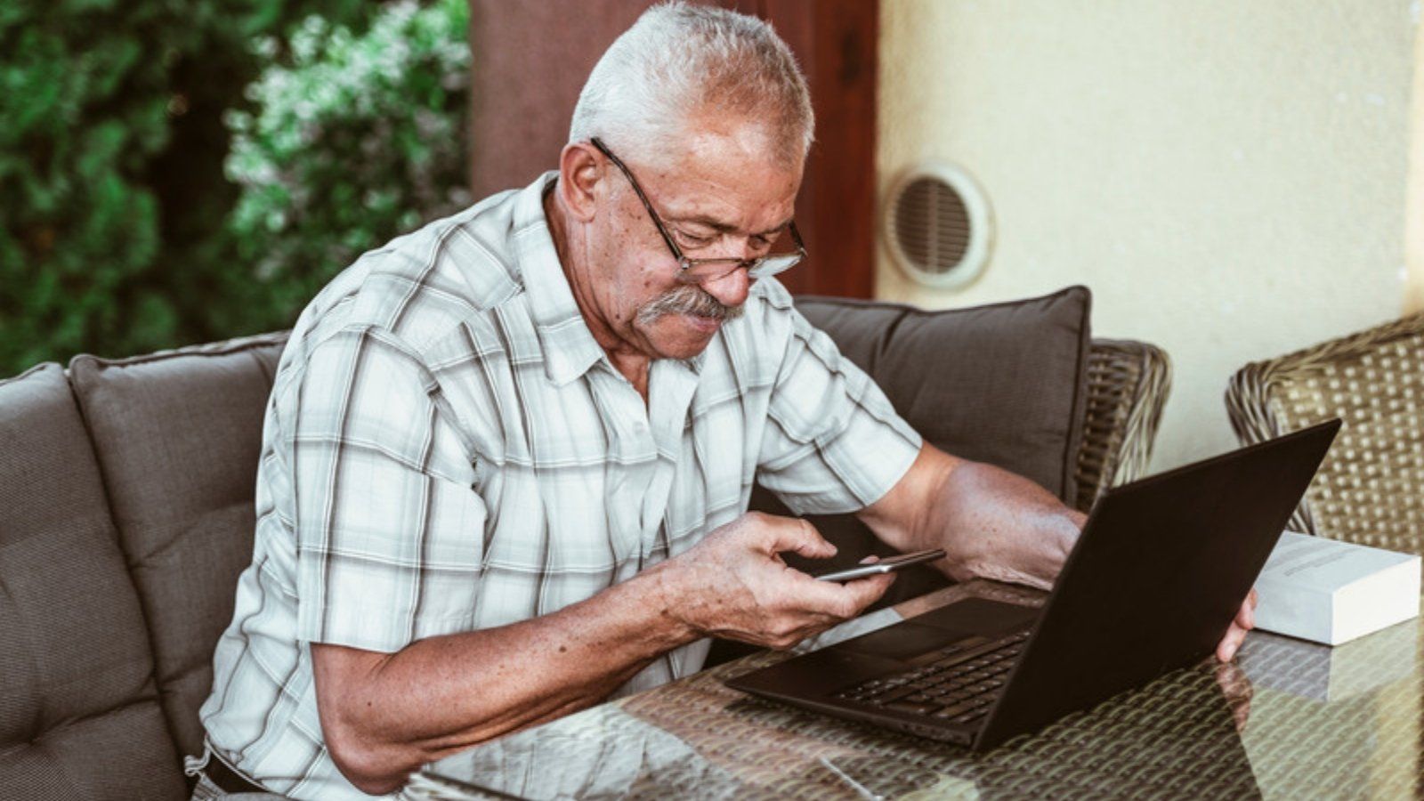 Older man checking a charity appeal on his phone beside a laptop before donating online