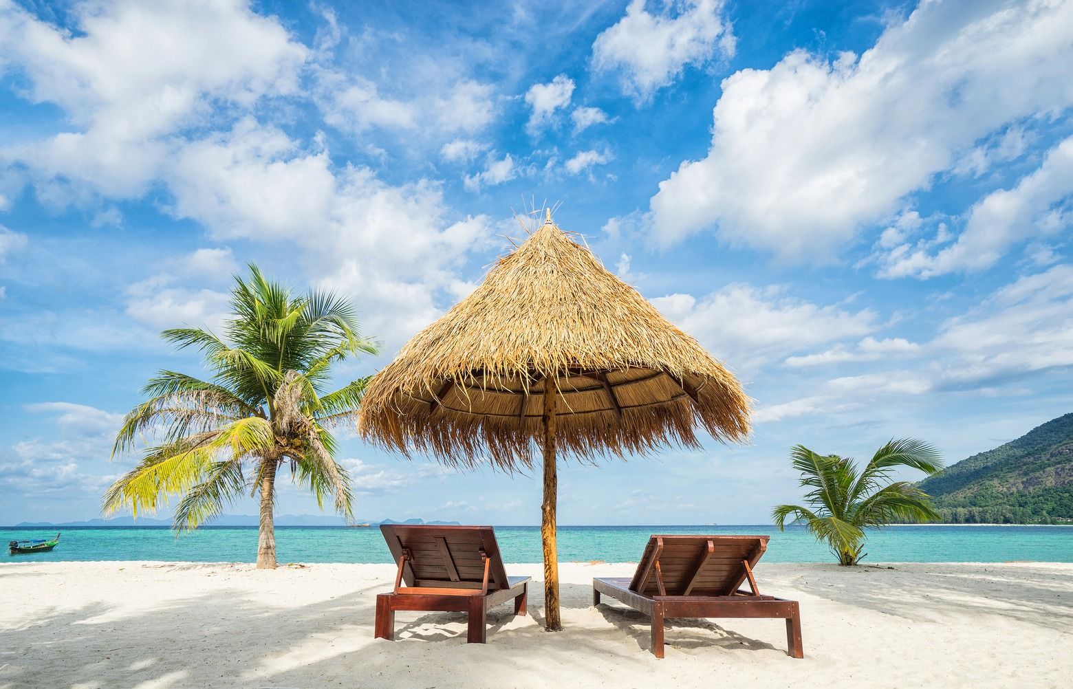 Two wooden lounge chairs under a thatched umbrella on a white sandy beach with palm trees, turquoise ocean, and a bright blue sky. Two wooden lounge chairs under a thatched umbrella on a white sandy beach with palm trees, turquoise ocean, and a bright blue sky.