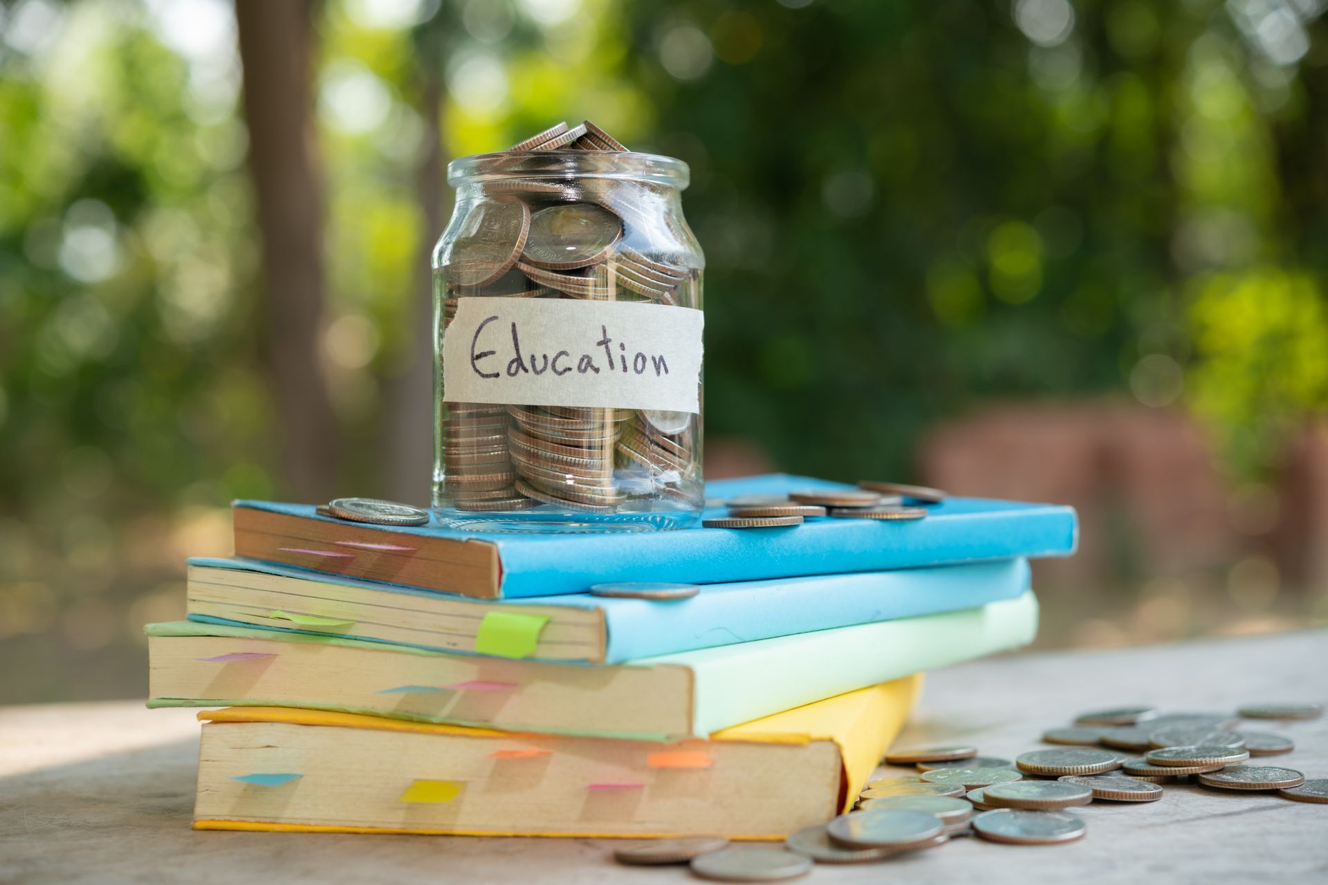 Un bocal en verre rempli de pièces étiquetées « Éducation » repose sur une pile de livres colorés. Un bocal en verre rempli de pièces étiquetées « Éducation » repose sur une pile de livres colorés.