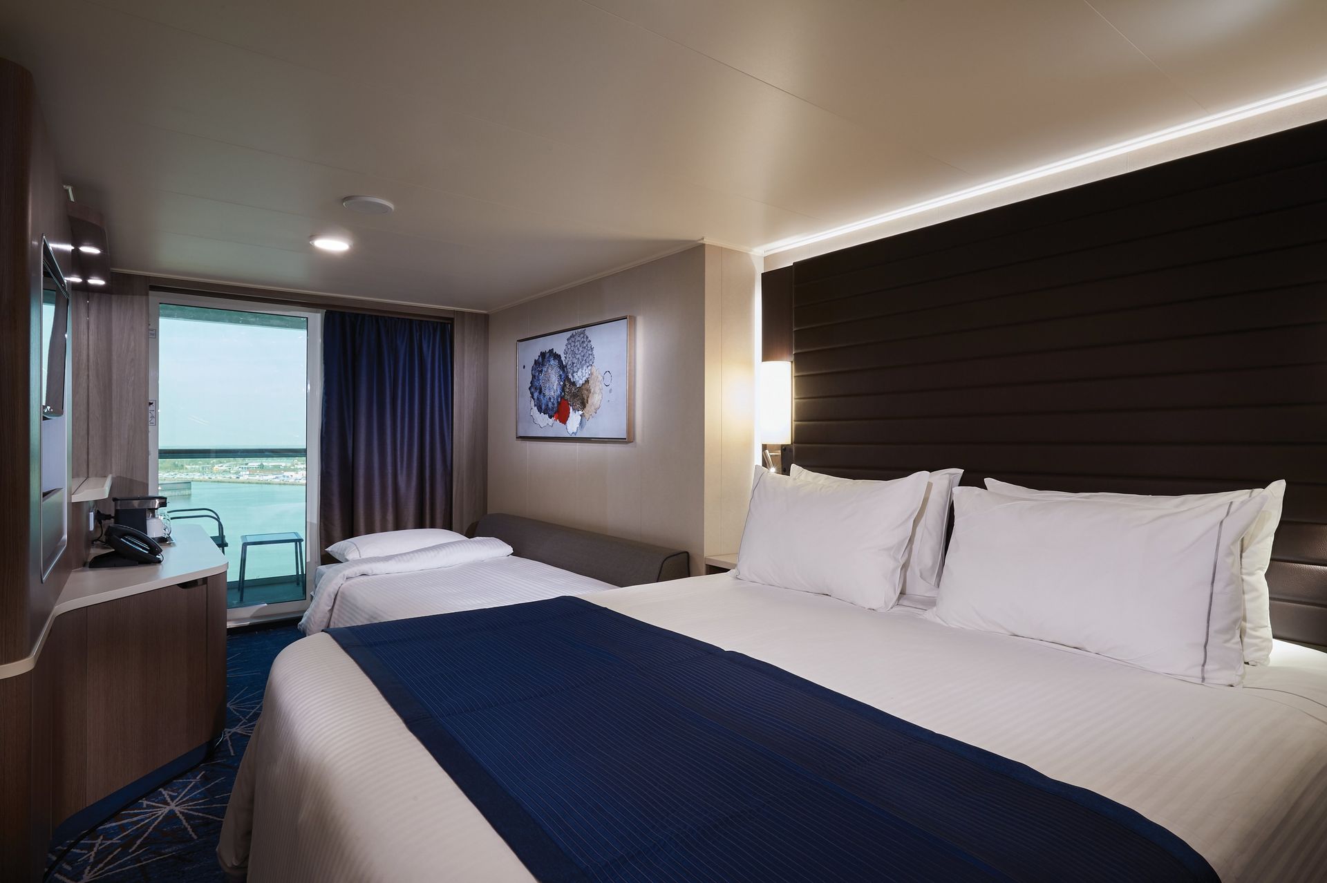 NCL balcony stateroom with a comfortable bed, private balcony, seating area, and beautiful ocean views.