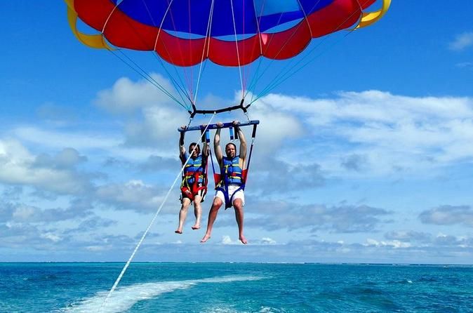 Two people parasailing over the turquoise ocean in Punta Cana under a colorful parachute on a sunny day.