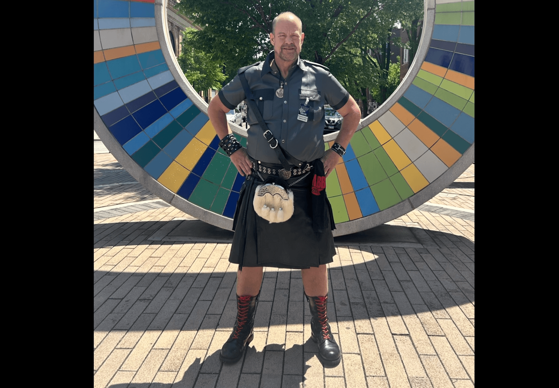 Scottie J standing confidently in full leather and kilt regalia in front of a large colorful circular mosaic sculpture in Chicago during IMLBB weekend Scottie J standing confidently in full leather and kilt regalia in front of a large colorful circular mosaic sculpture in Chicago during IMLBB weekend