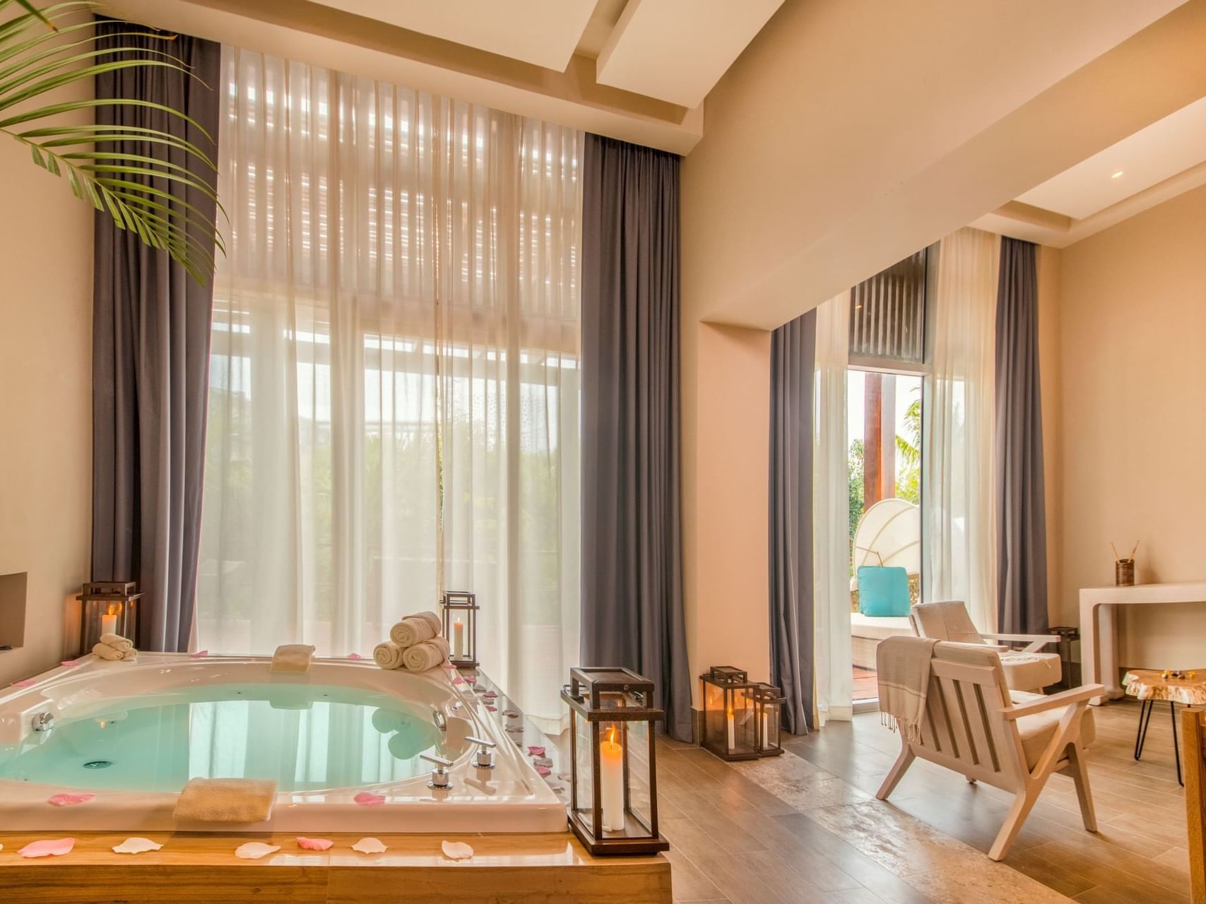 Luxury Spa Journey Suite at Haven Riviera Cancun featuring a private indoor Jacuzzi with rose petals, tall sheer curtains, cozy lounge chairs, and warm ambient lighting for a romantic wellness retreat. 