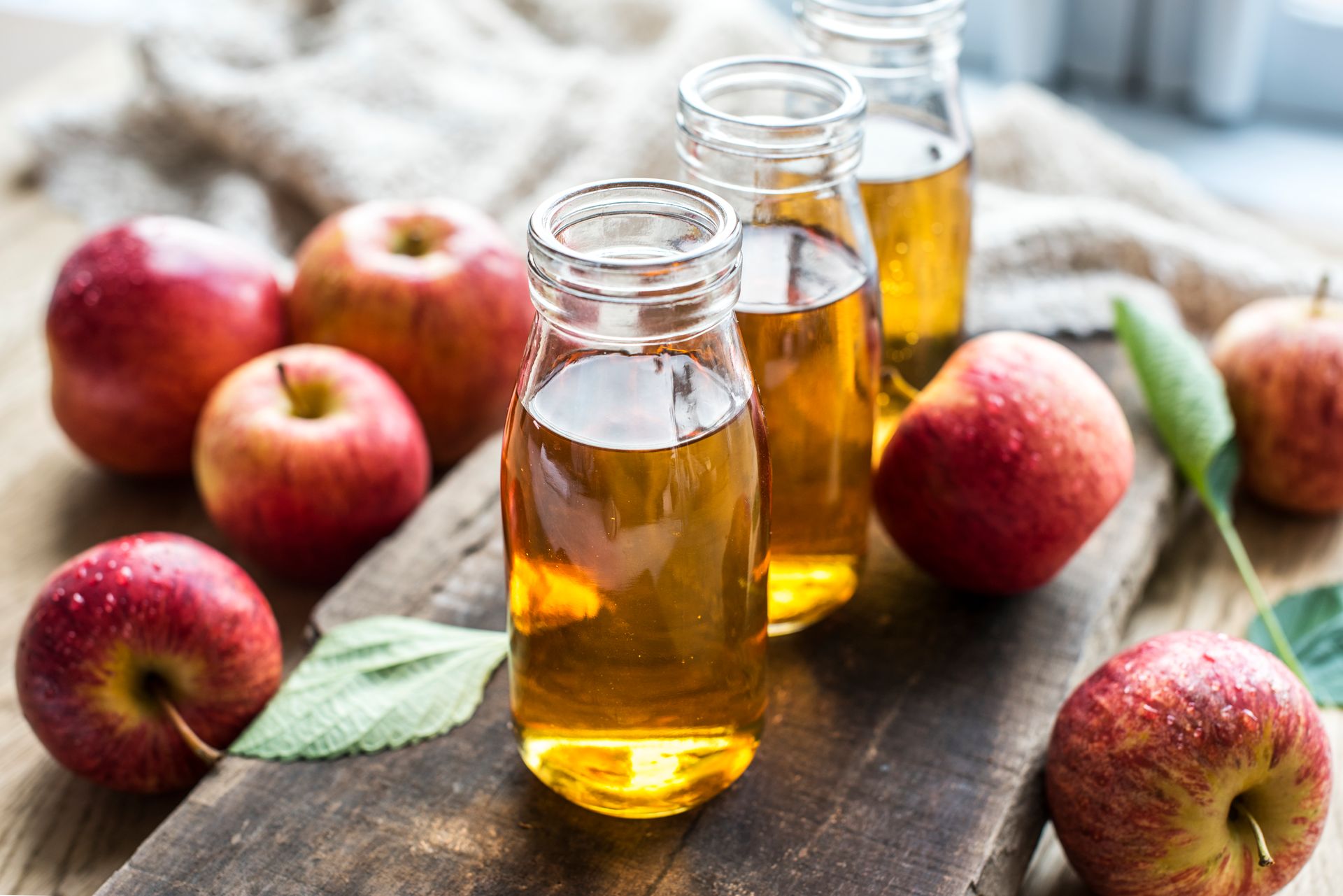 petite bouteille de vinaigre de cidre, plusieurs pommes poser sur une table en bois