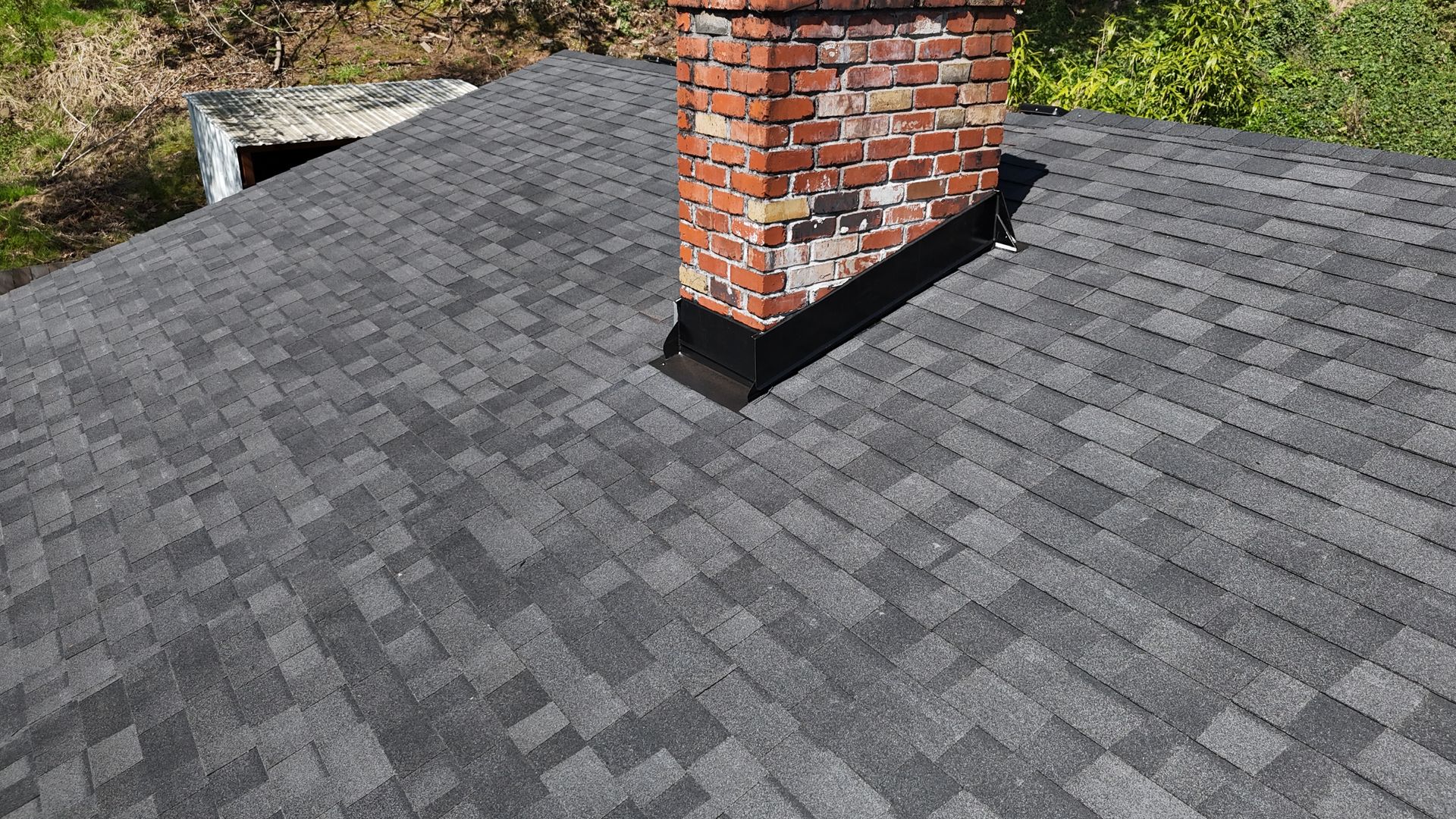 Shingle roof and metal flashing at the base of a brick chimney.