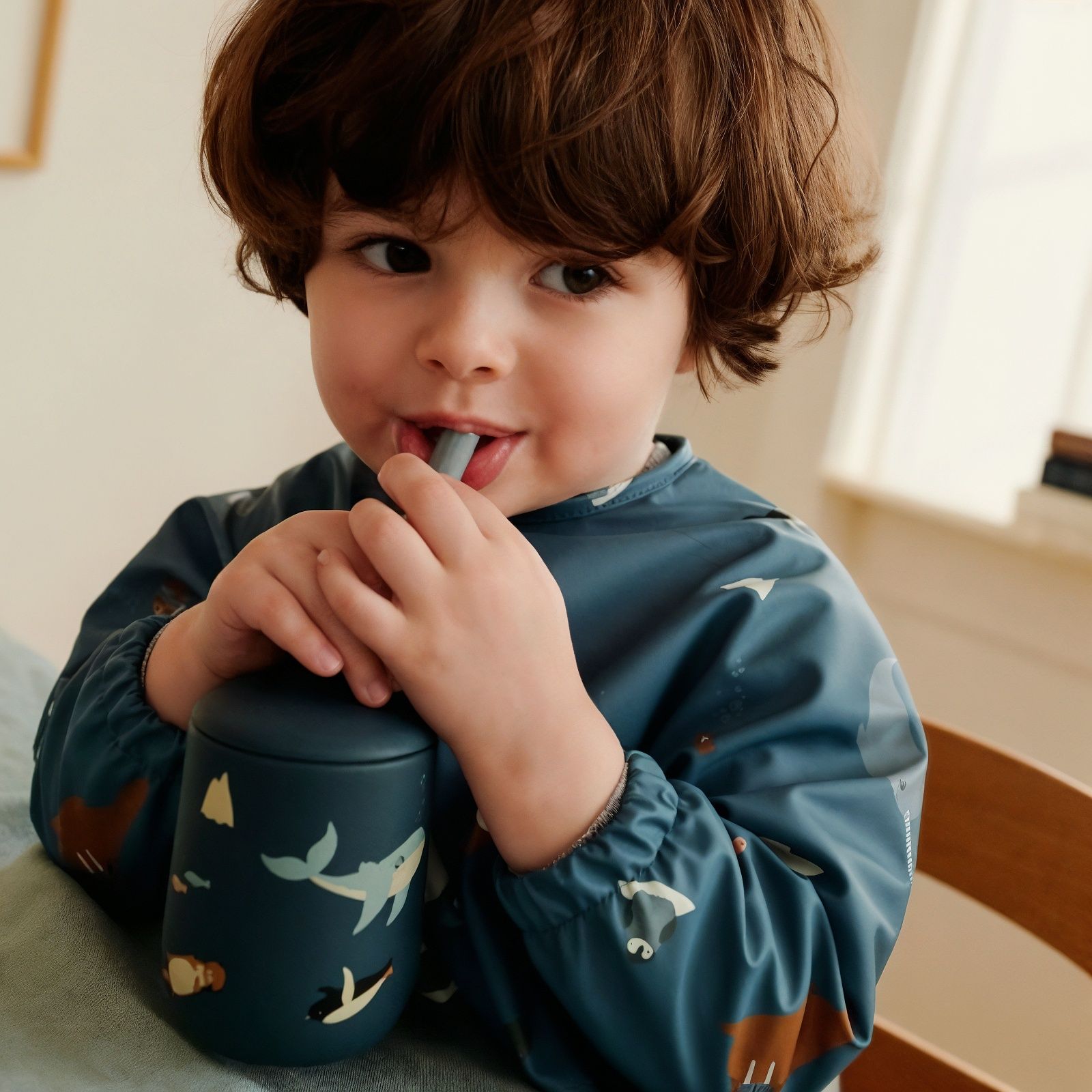 Bébé buvant sans sa gourde, portant un bavoir tablier. Bébé buvant sans sa gourde, portant un bavoir tablier.
