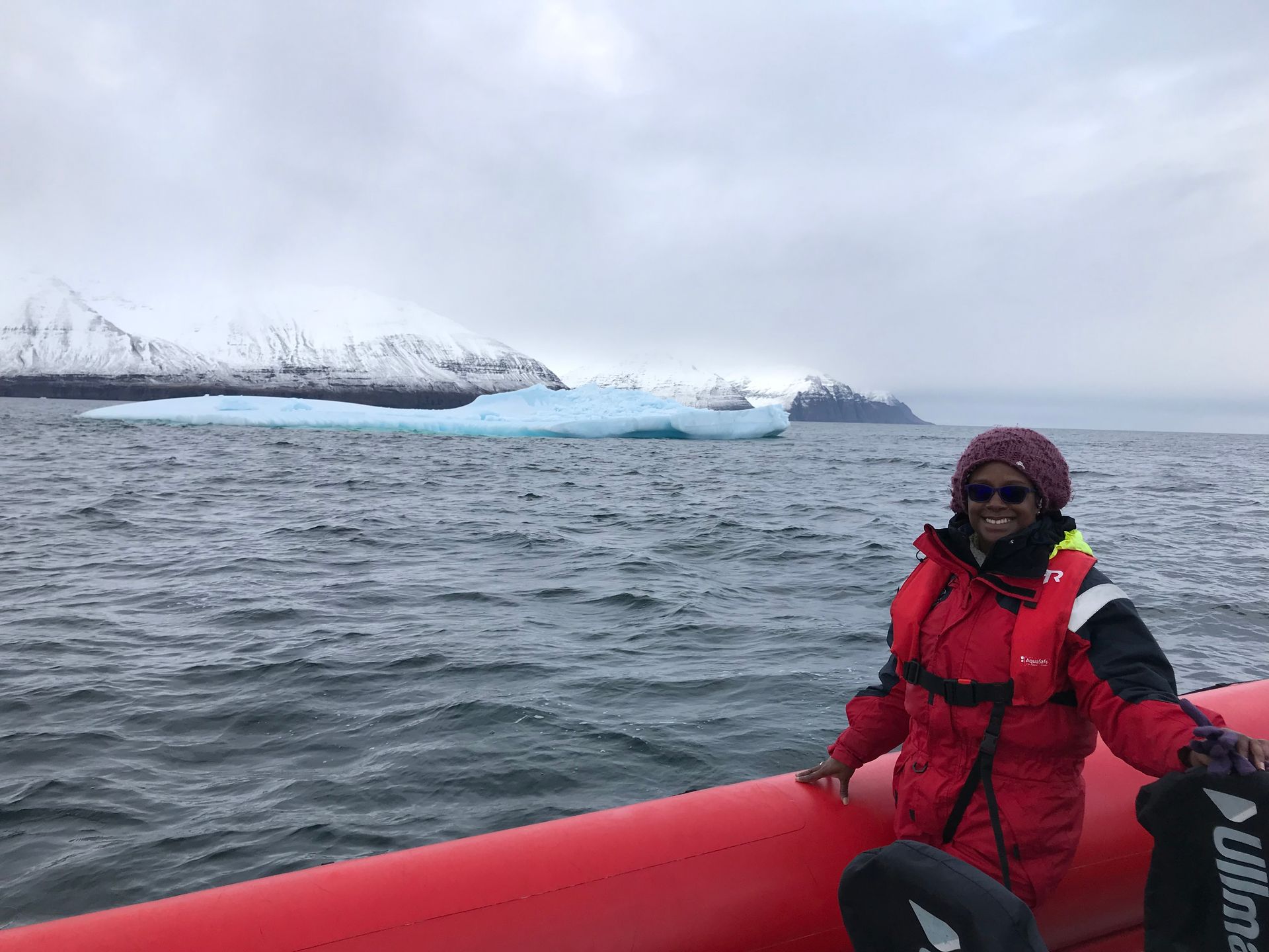 Michelle Green on a solo trip in Iceland, smiling from a boat with an iceberg and snow-covered mountains in the background.