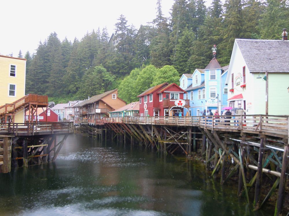Colorful historic buildings line the waterfront on wooden pilings in Ketchikan, Alaska, surrounded by lush evergreen forests and calm harbor waters on a misty day. Colorful historic buildings line the waterfront on wooden pilings in Ketchikan, Alaska, surrounded by lush evergreen forests and calm harbor waters on a misty day.