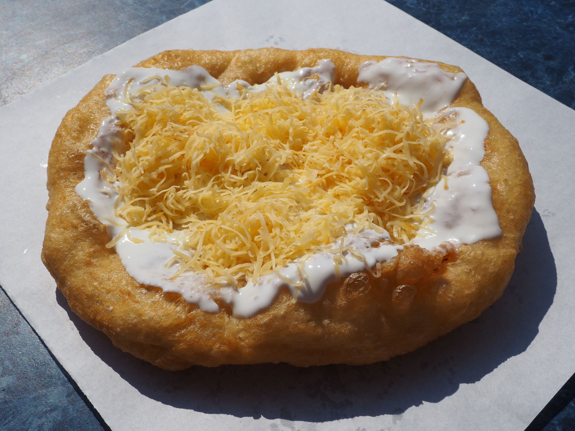A freshly made Hungarian lángos topped with sour cream and a generous layer of shredded cheese, served on parchment paper. This popular Christmas market comfort food is a favorite on German Christmas river cruises and throughout Central Europe. A freshly made Hungarian lángos topped with sour cream and a generous layer of shredded cheese, served on parchment paper. This popular Christmas market comfort food is a favorite on German Christmas river cruises and throughout Central Europe.
