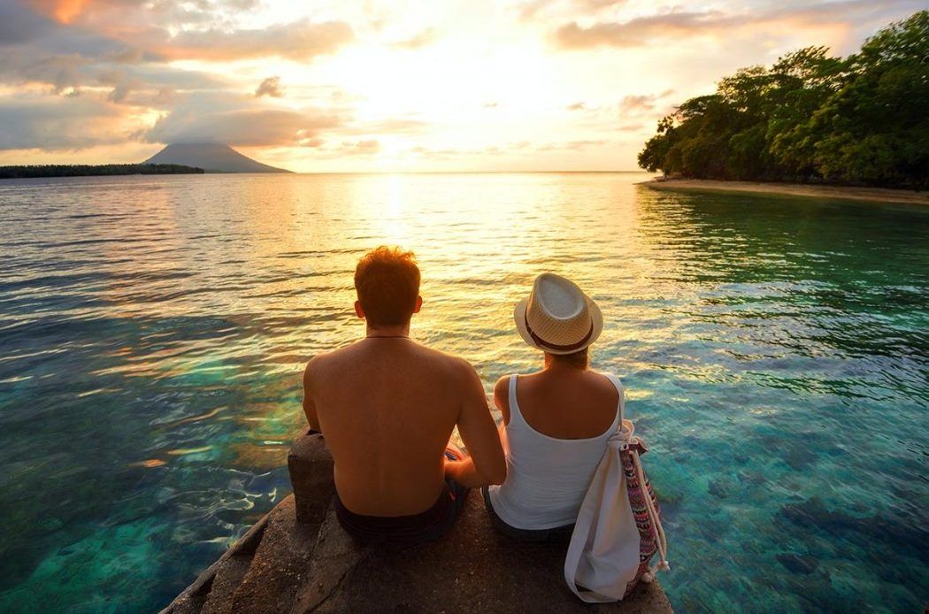 Couple sitting by the ocean at sunset, enjoying a romantic view.