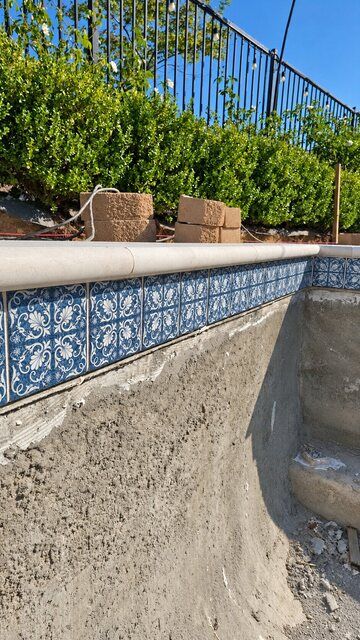 Blue and white patterned waterline tile with light stone pool coping during construction