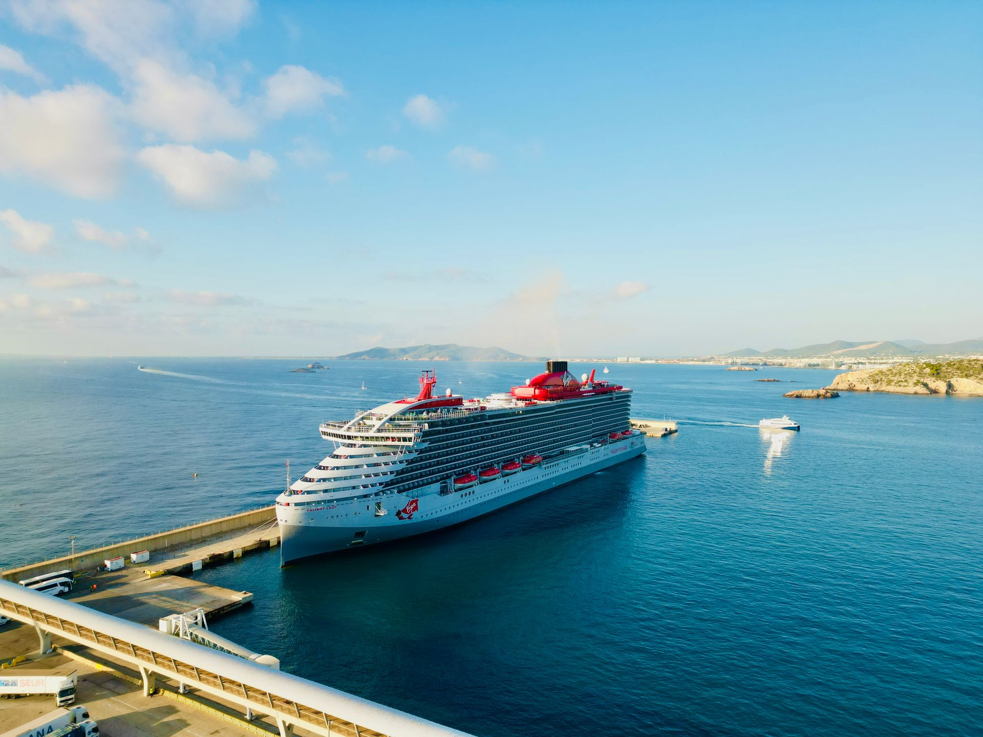 irgin Voyages cruise ship docked at a scenic Mediterranean port with calm blue waters and a clear sky. irgin Voyages cruise ship docked at a scenic Mediterranean port with calm blue waters and a clear sky.