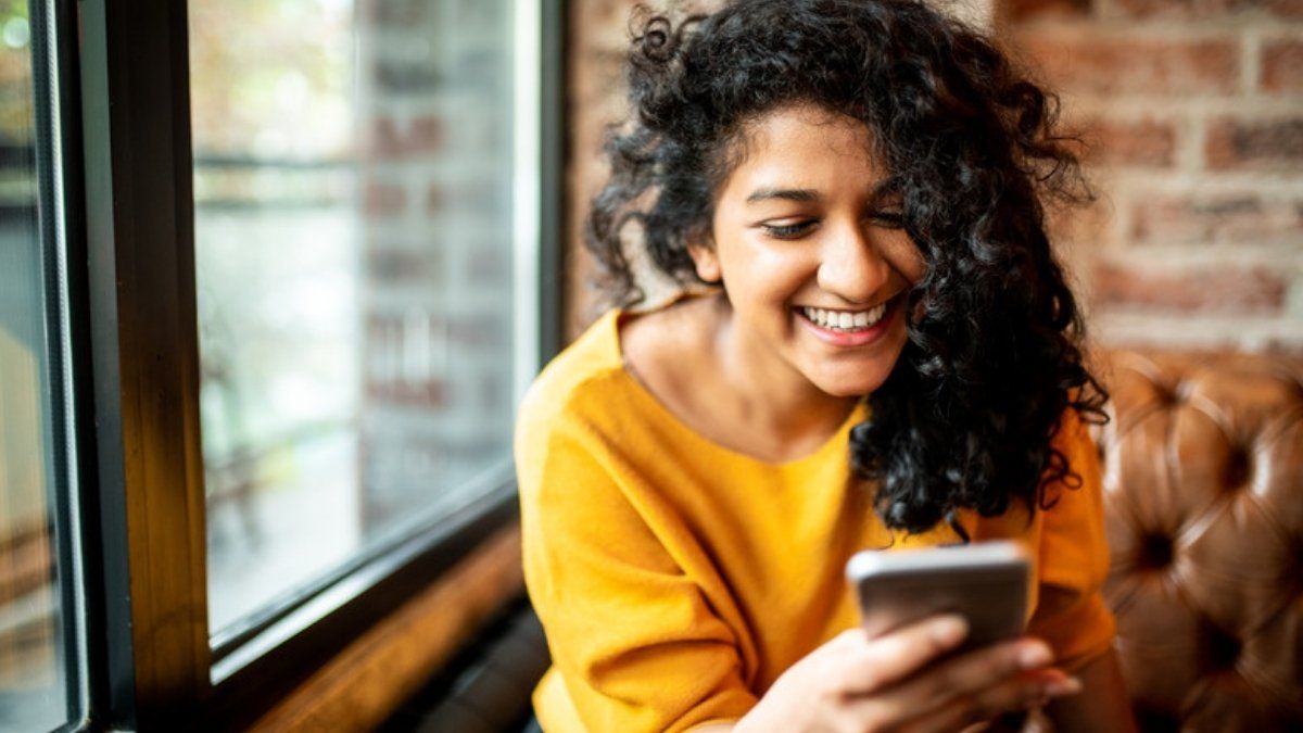 Smiling woman reading a message on her phone, an example of a polished AI-written scam message