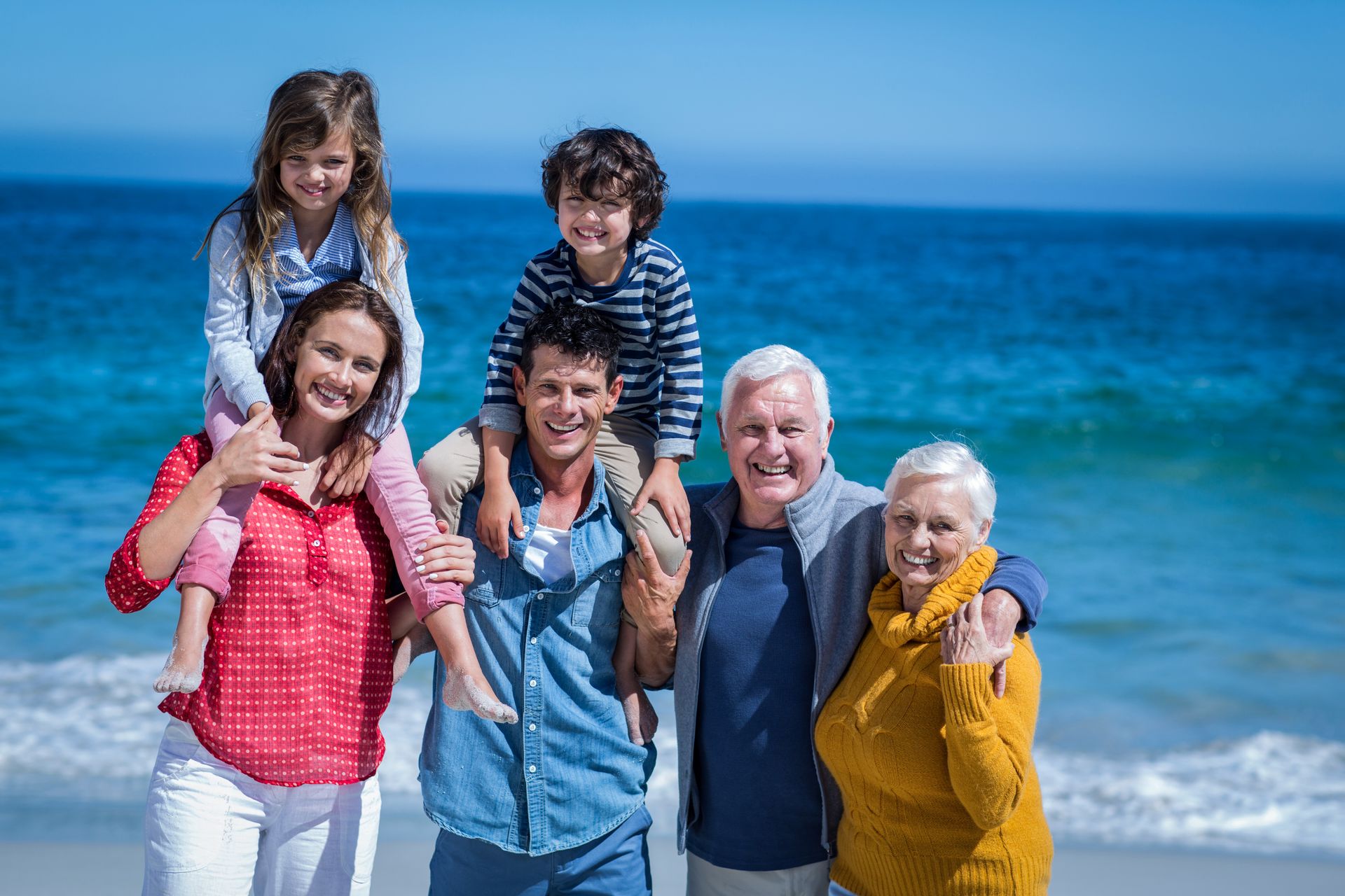 Smiling multigenerational family standing together on a sunny beach, enjoying time by the ocean.