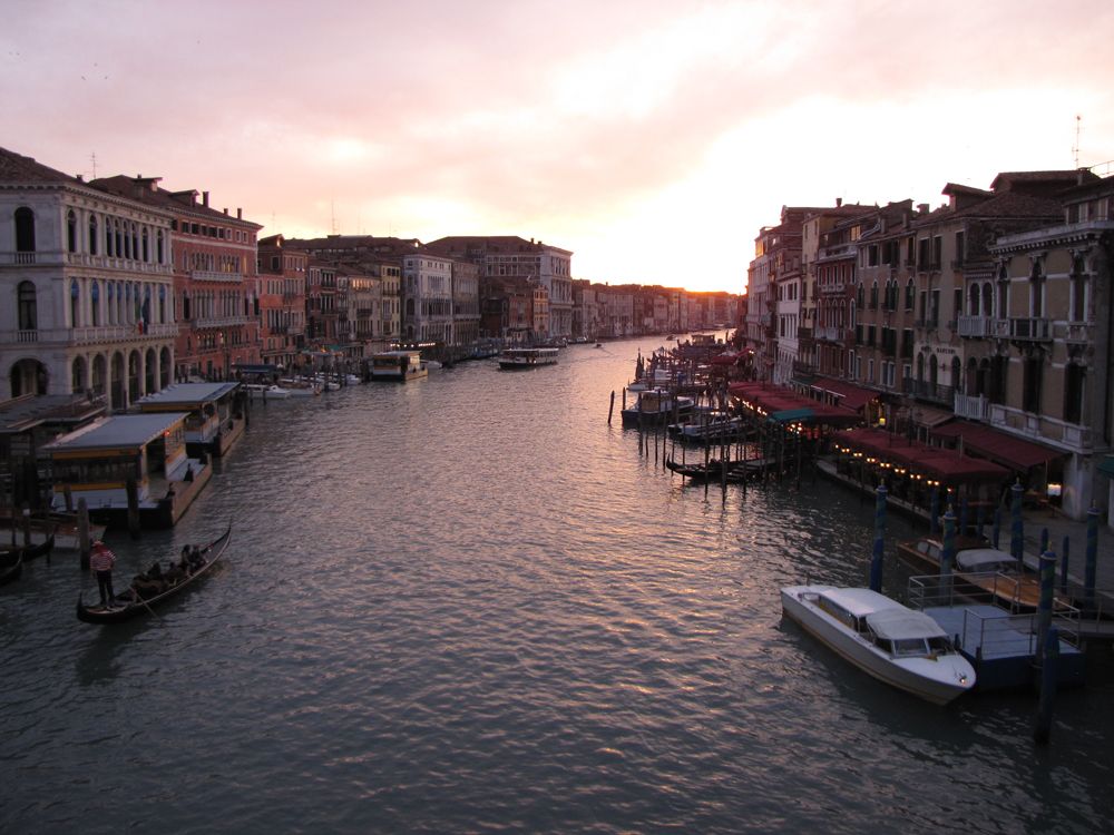 Sunset over the Grand Canal in Venice, Italy, with historic buildings lining the water, gondolas and boats cruising the canal, and a colorful evening sky. Sunset over the Grand Canal in Venice, Italy, with historic buildings lining the water, gondolas and boats cruising the canal, and a colorful evening sky.
