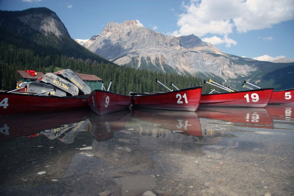 Red canoes lined up along the shore of Emerald Lake in Yoho National Park, British Columbia, with clear water, evergreen forests, and towering Rocky Mountains in the background. Red canoes lined up along the shore of Emerald Lake in Yoho National Park, British Columbia, with clear water, evergreen forests, and towering Rocky Mountains in the background.