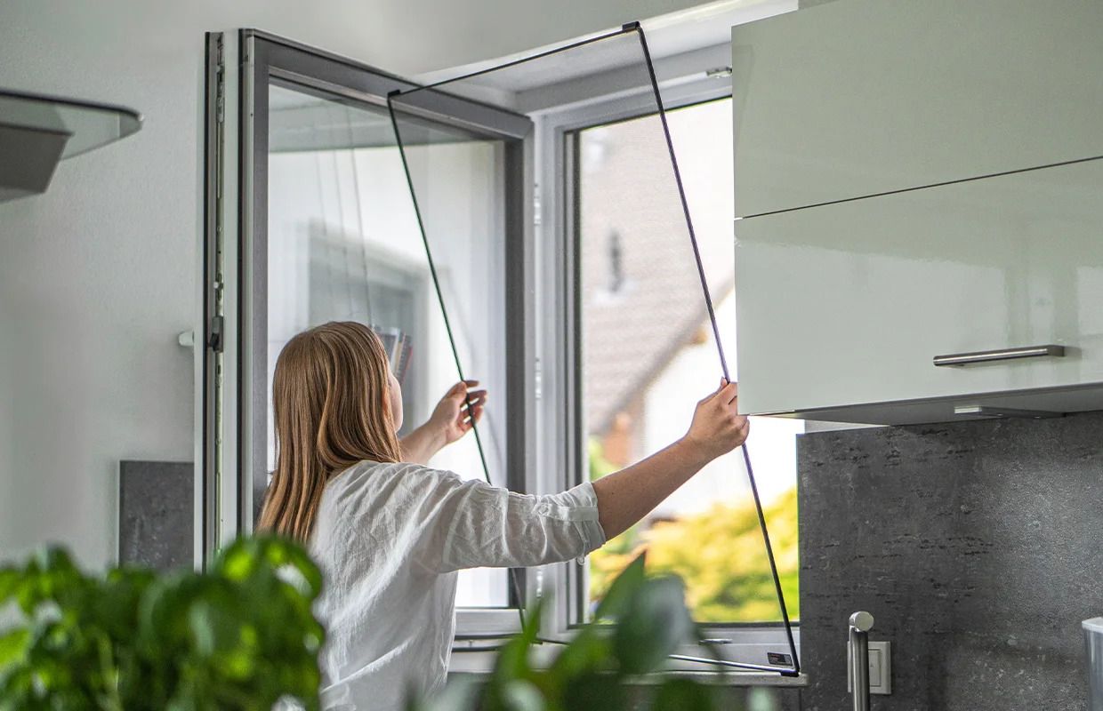 Frau setzt den flexiblen FlexScreen-Insektenschutzrahmen in ein Küchenfenster ein