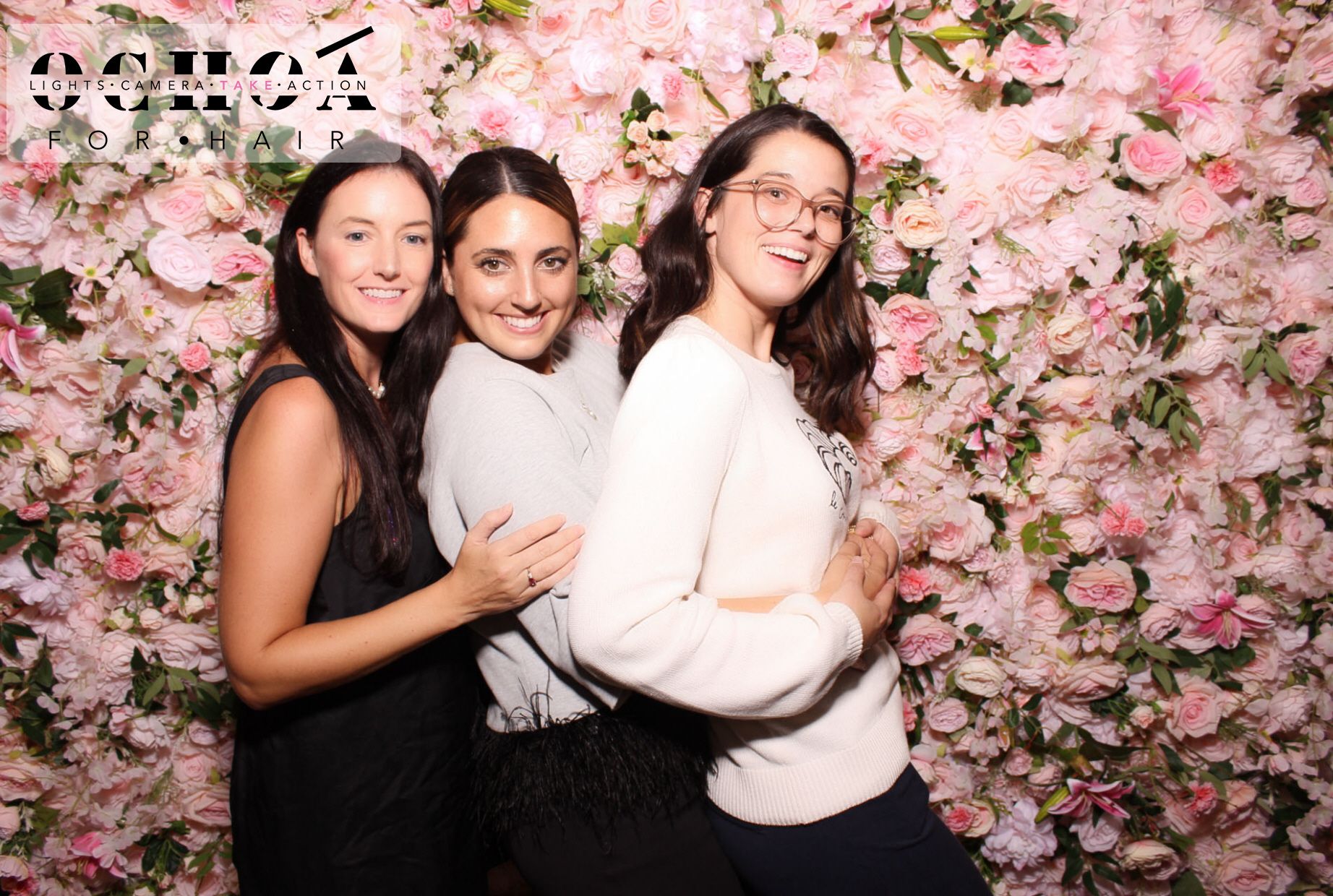 Three people posing with props at a photo booth against a purple patterned backdrop.