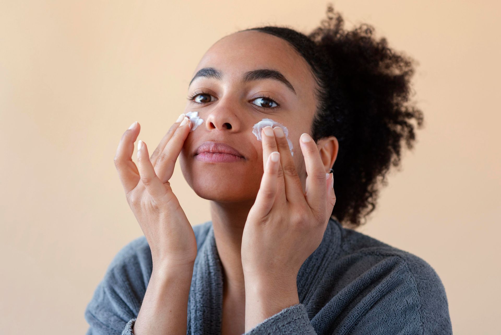 Une femme applique une crème sur son visage, profitant d'un moment de soin personnel. Une femme applique une crème sur son visage, profitant d'un moment de soin personnel.