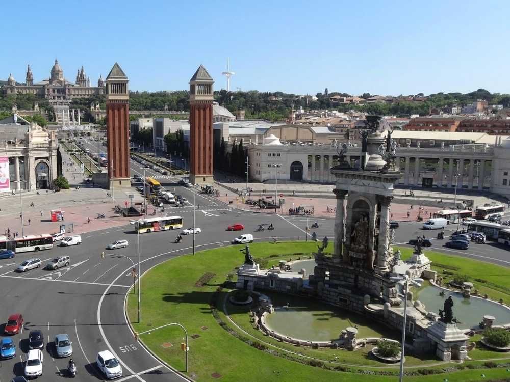 Vista superior da Praça de Espanya, uma grande rotatória gramada com escultura e espelho d'agua ao centro