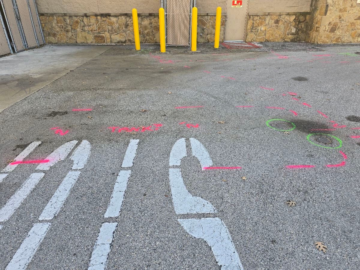 Pavement marked with locate paint showing multiple underground utility runs