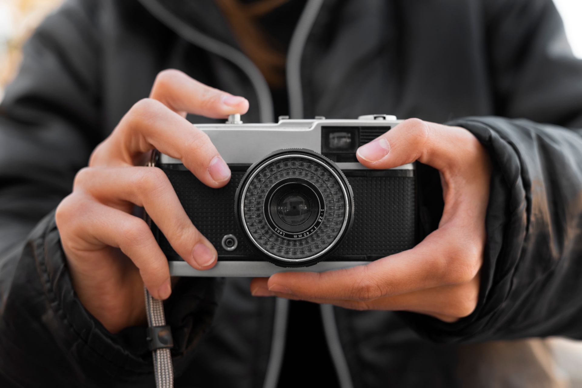 Gros plan de mains tenant un appareil photo argentique vintage avec un objectif texturé, encadré par une veste sombre, transmettant concentration et nostalgie. Gros plan de mains tenant un appareil photo argentique vintage avec un objectif texturé, encadré par une veste sombre, transmettant concentration et nostalgie.