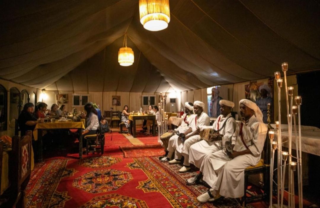Group of friends having dinner with traditional music in a luxury tent deep in marzouga desert 