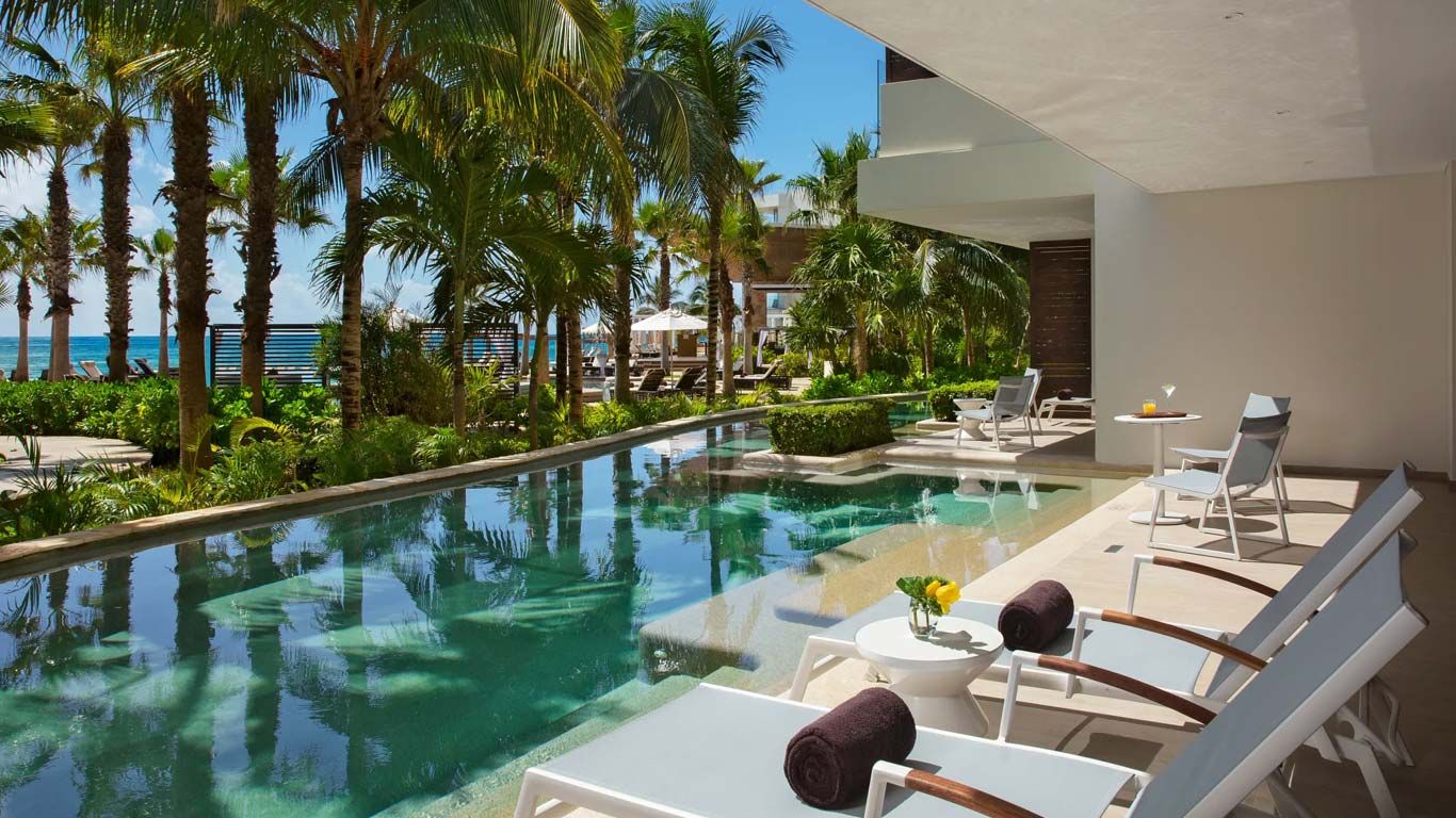 Luxury resort pool with palm trees and lounge chairs near the beach