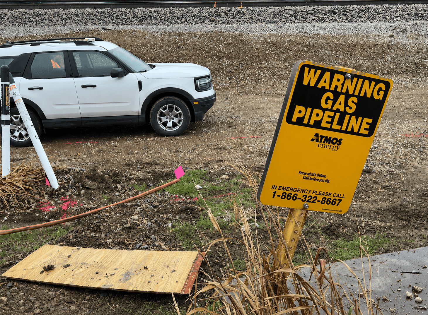 Warning gas pipeline sign near active underground utility locating and excavation work adjacent to railroad tracks and a utility access Warning gas pipeline sign near active underground utility locating and excavation work adjacent to railroad tracks and a utility access