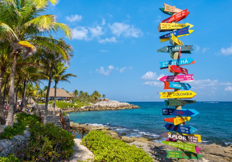 Colorful directional signpost on a tropical coastline with palm trees, clear blue sky, and turquoise ocean in the background, symbolizing travel and exploration. Colorful directional signpost on a tropical coastline with palm trees, clear blue sky, and turquoise ocean in the background, symbolizing travel and exploration.