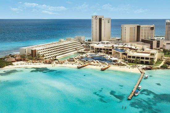 Aerial view of Hyatt Ziva Cancun all-inclusive resort with white sand beach, turquoise Caribbean waters, multiple pools, beachfront buildings, and wooden pier extending into the ocean