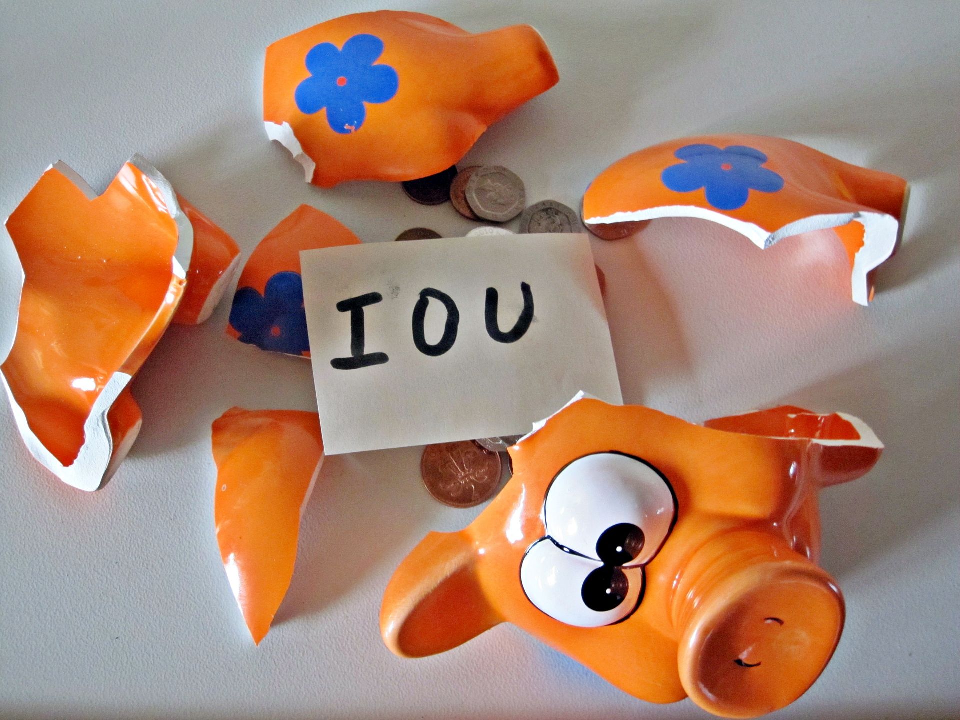 Broken orange piggy bank with coins scattered around it and a handwritten “IOU” note on top.