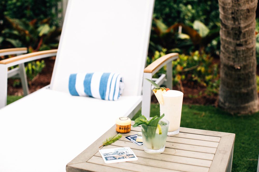 Refreshing tropical cocktails on a poolside lounge table beside a white sunbed with a rolled towel, surrounded by lush greenery. Refreshing tropical cocktails on a poolside lounge table beside a white sunbed with a rolled towel, surrounded by lush greenery.