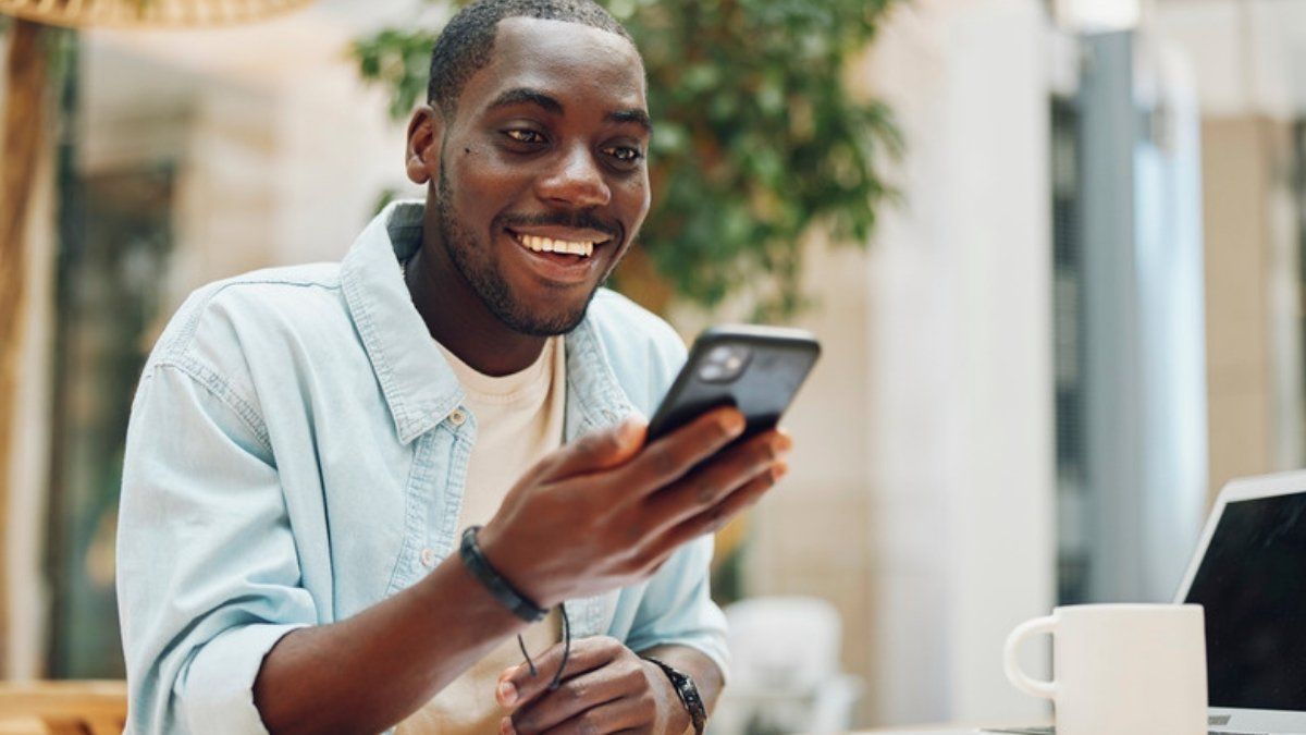 Smiling man using a phone and laptop, showing how to stay safe online with simple everyday habits