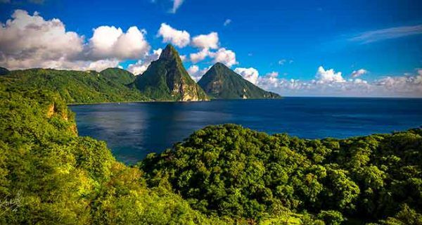 Scenic view of Saint Lucia’s famous Pitons rising above the blue Caribbean Sea, surrounded by lush tropical forest under a bright sky.