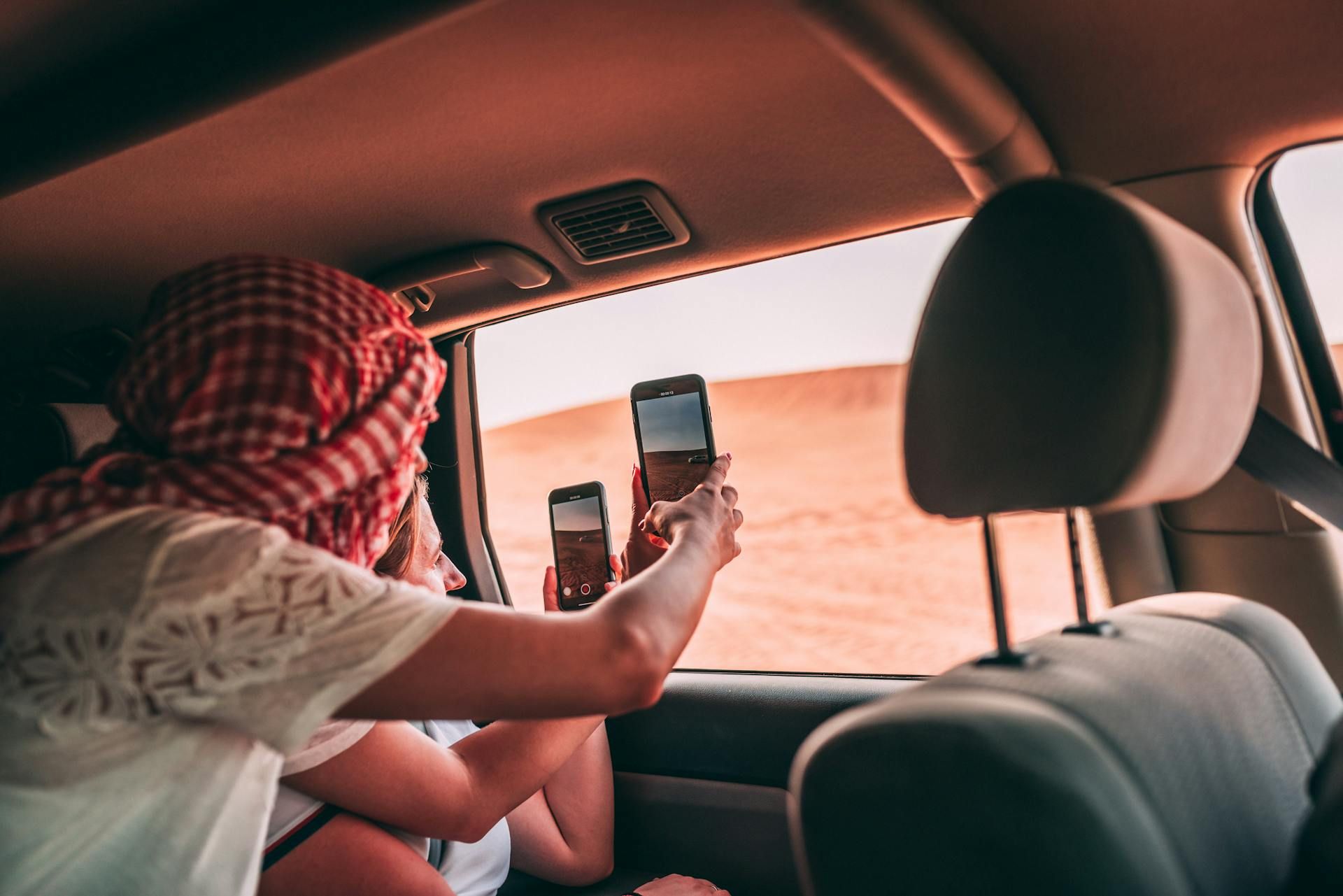 Two Women Using Their Phones To Take Photos of Dubai's Desert In The Daytime Two Women Using Their Phones To Take Photos of Dubai's Desert In The Daytime