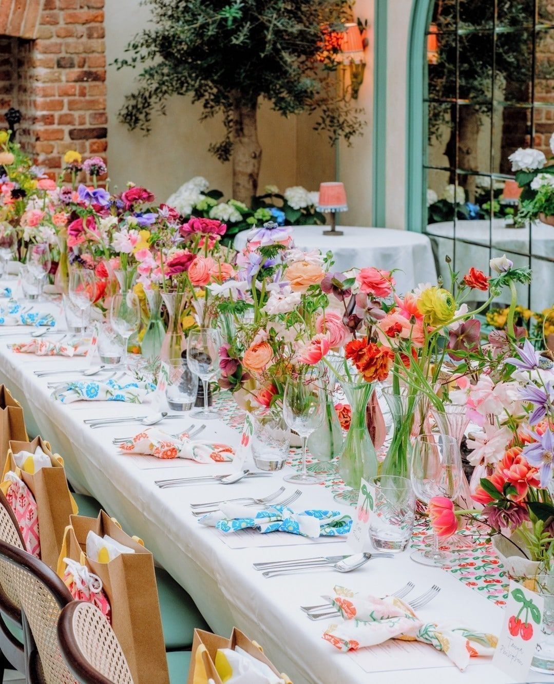 Colorful wedding reception table in Antalya Turkey decorated with vibrant summer flowers, glassware, and gift bags in a garden setting Colorful wedding reception table in Antalya Turkey decorated with vibrant summer flowers, glassware, and gift bags in a garden setting