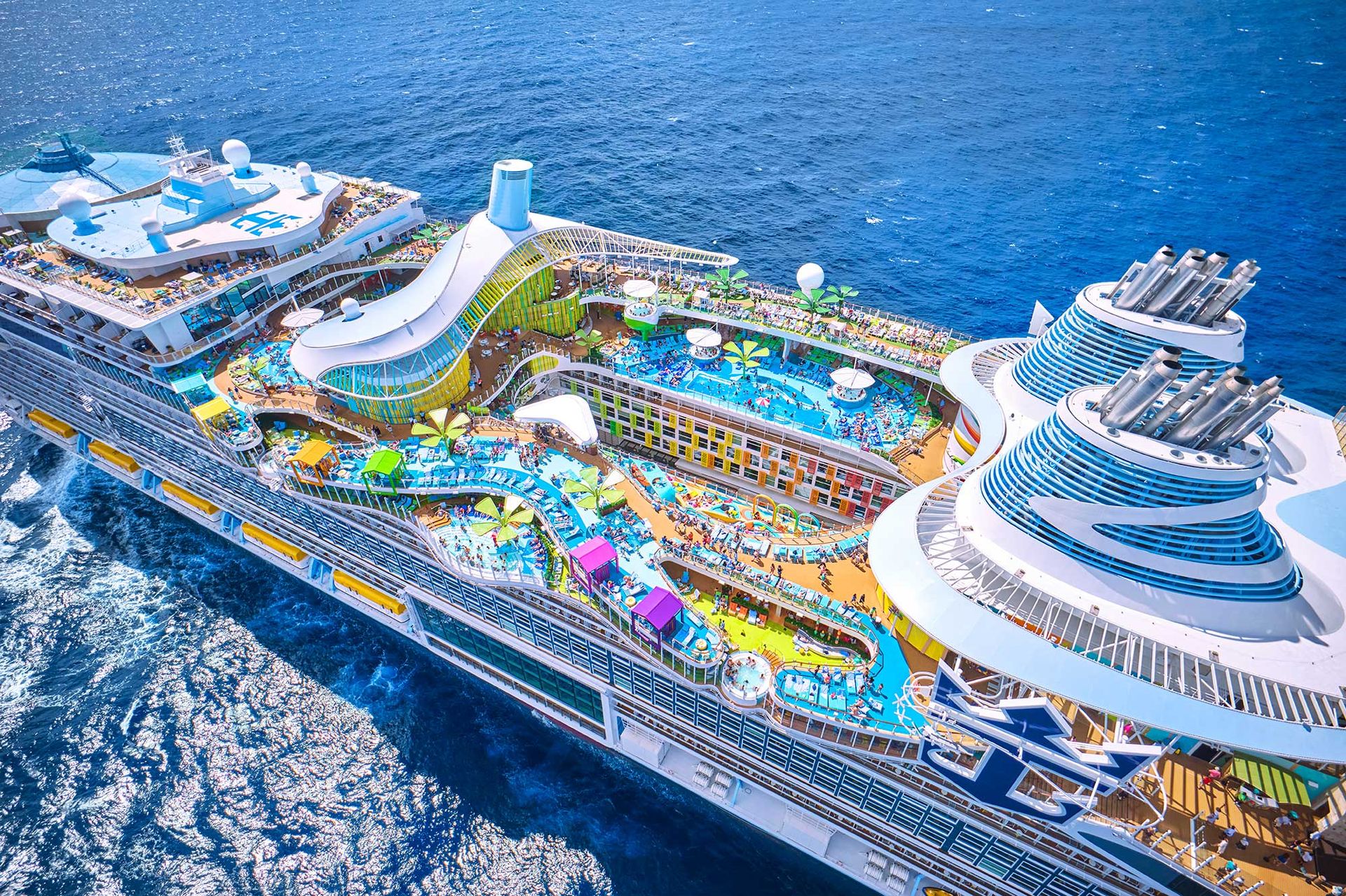 A vibrant cruise ship at sea with colorful pools, decks, and ocean views under a bright blue sky, filled with guests enjoying the experience.