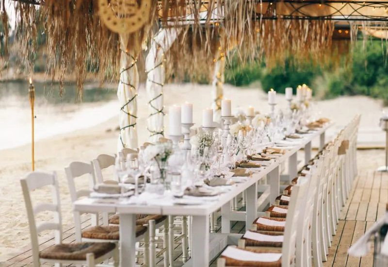 Elegant beach wedding setup in Antalya Turkey with a long white table, rustic canopy, candles, and a seaside view Elegant beach wedding setup in Antalya Turkey with a long white table, rustic canopy, candles, and a seaside view