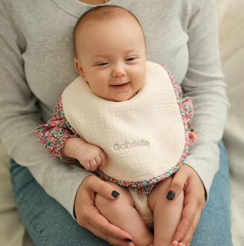 un bébé assis sur sa mère portant un bavoir qui sourit devant l'objectif. un bébé assis sur sa mère portant un bavoir qui sourit devant l'objectif.