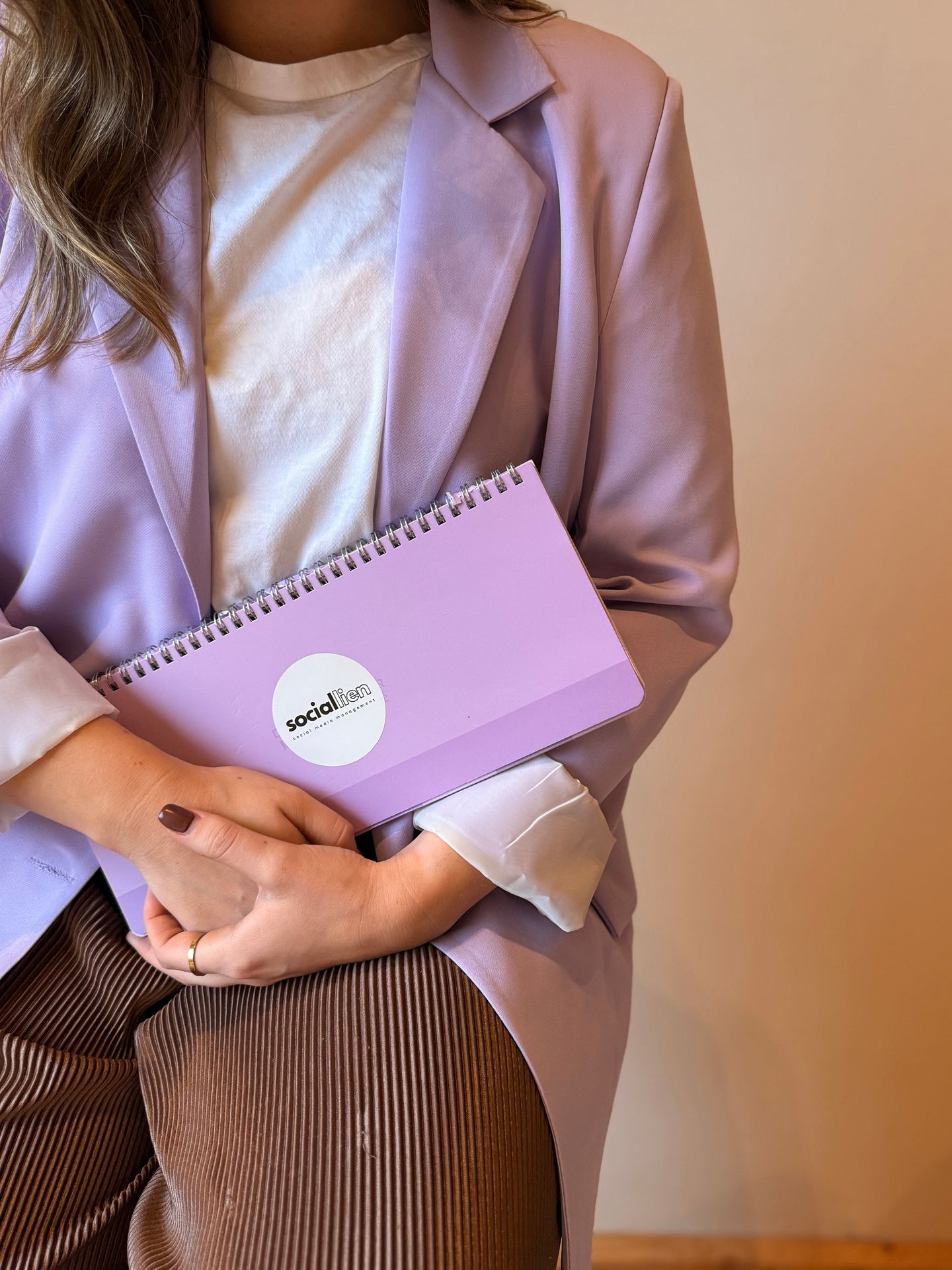 Person in lavender blazer holding a purple notebook with 'socialflair' on the cover.